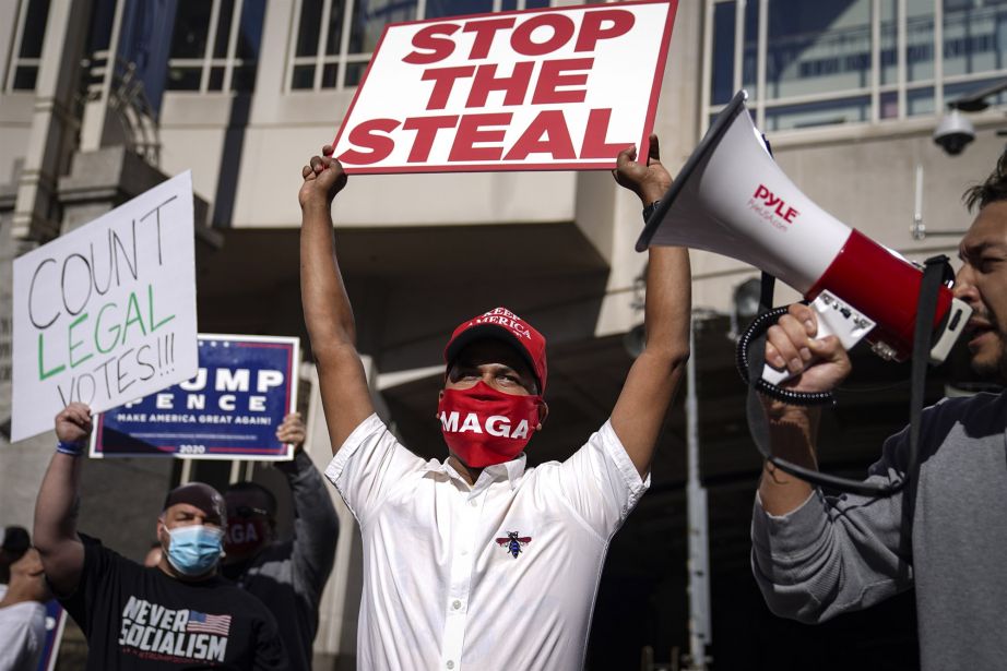 A demonstrator stands with supporters of President Donald Trump outside the Pennsylvania Convention Center