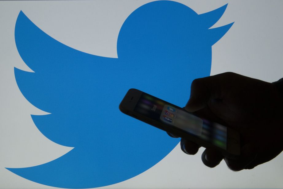 A picture shows a man holding a cellphone in front of the Twitter logo on March 16, 2017. (Photo by Gokhan Balci/Anadolu Agency/Getty Images)