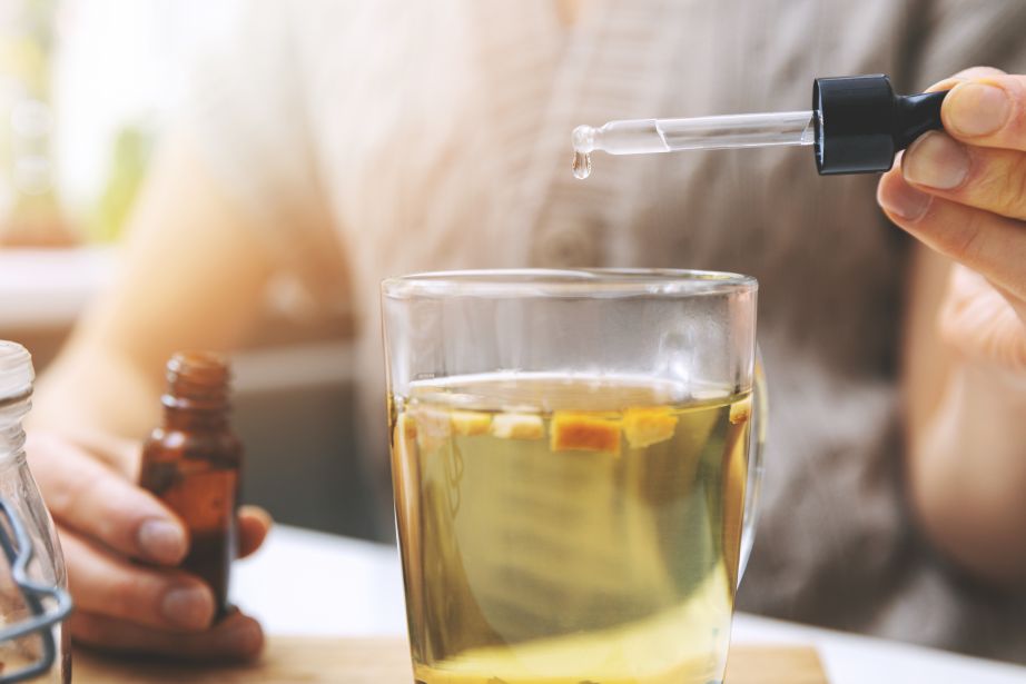 dietary supplements and vitamins - woman adding drops in cup of tea with dropper