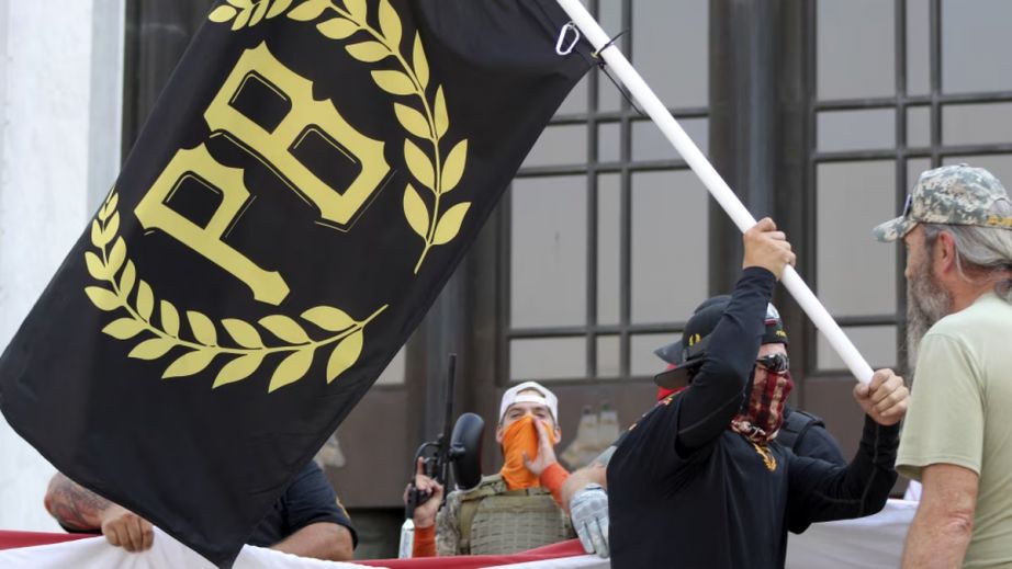 A protester carries a Proud Boys banner, a right-wing group, while other members start to unfurl a large U.S. flag in front of the Oregon State Capitol in Salem, Oregon.